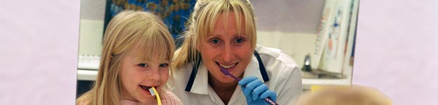 Photo of a dental nurse showing a child how to brush her teeth