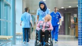 healthcare professional pushing a woman in a wheelchair down a hospital corridor