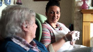 A woman having tea with a care worker in her home